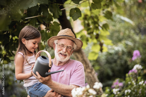 Little girl helping her grandpa watering plants photo