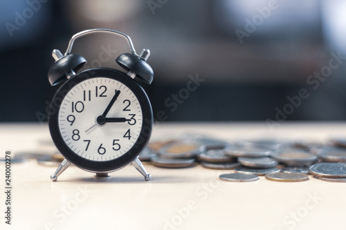 Alarm clock and many coins with copy space on wooden top view. selected focus at clock.