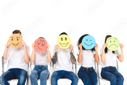 multicultural friends in blue jeans sitting on chairs and holding multicolored signs isolated on white