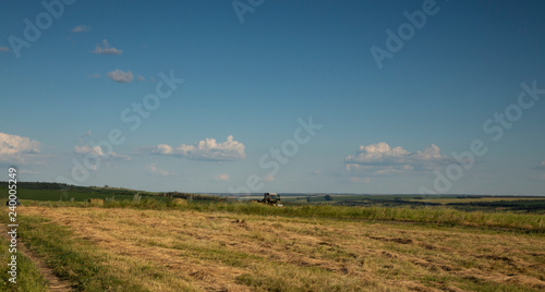 Agricultural machinery removes hay and bales in the fields. Clear sunny summer weather.