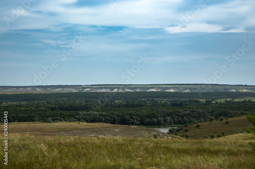 View of the forest and fields, chalk mountains from a small elevation on the plain. Beautiful clouds in the blue sky. Summer.