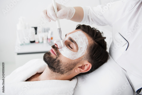 Bearded man smiling and having white mask on his face in spa