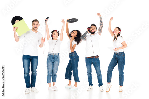 multicultural group of young people with raised hands listening music in headphones and holding vinyl records isolated on white