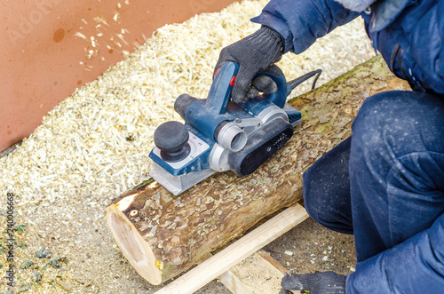 male carpenter grinds a log with a hand-held electric planer. Woodwork. Manufacture of wood products. Carpentry workshop