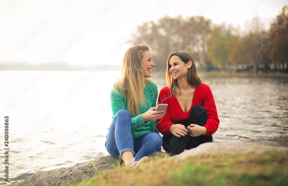 Fototapeta premium Friends listening music with earphones, sitting along the riverside