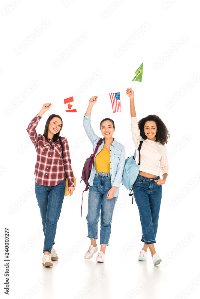 Obraz premium cheerful girls with flags of different countries above heads isolated on white