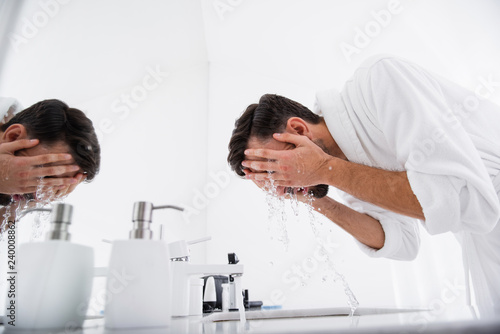 Dark haired man closing his face with hands while washing it