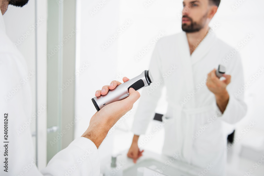Man in bathrobe standing and holding shaving machine Man in bathrobe standing and holding shaving machine