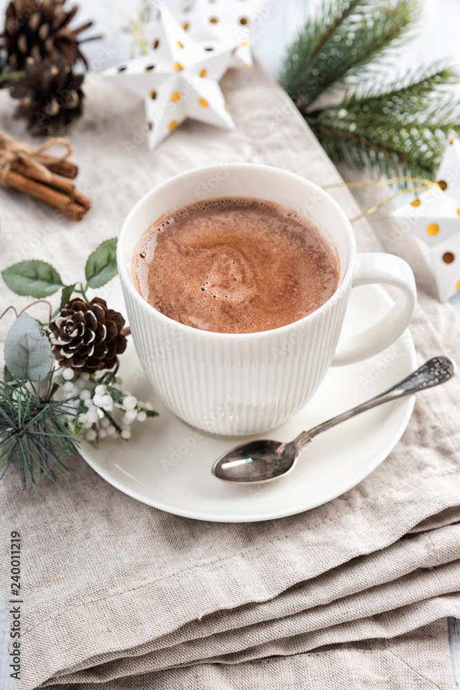 Cup of hot chocolate with cinnamon sticks on the white wooden table. Winter cocoa drink on a napkin, Christmas-tree golden stars decorations, branches and cones Cup of hot chocolate with cinnamon sticks on the white wooden table. Winter cocoa drink on a napkin, Christmas-tree golden stars decorations, branches and cones