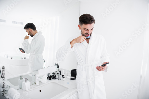 Emotional man brushing his teeth and looking at smartphone