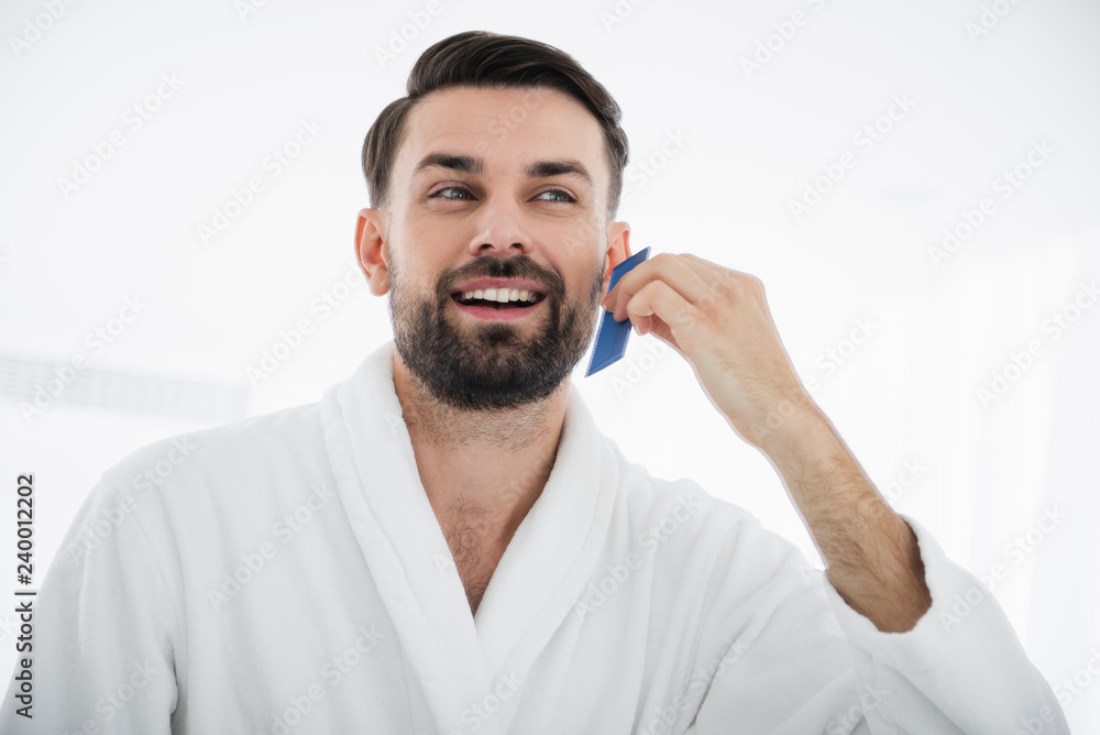 Close up of happy man combing beard and smiling