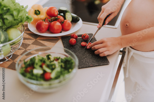 Pregnant woman holding knife and chopping tomatoes on salad