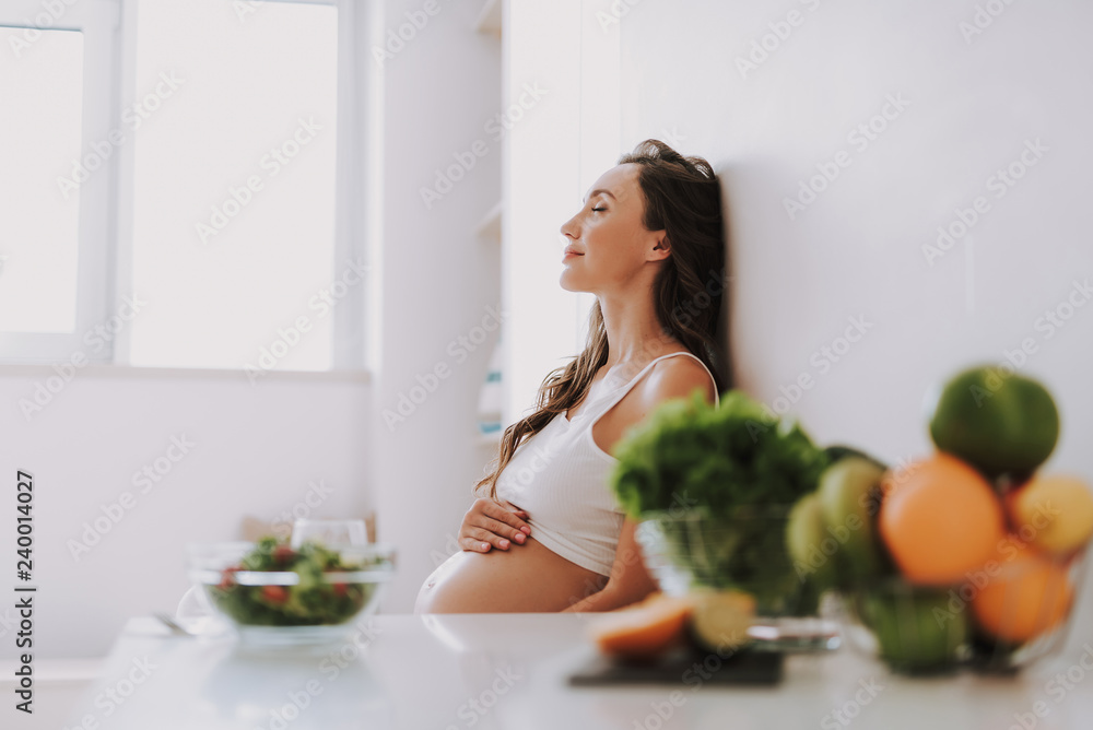 Calm expectant mama sitting on chair and holding hands on stomach