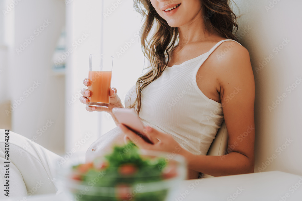 Young mum looking at cellular and holding glass of juice Young mum looking at cellular and holding glass of juice