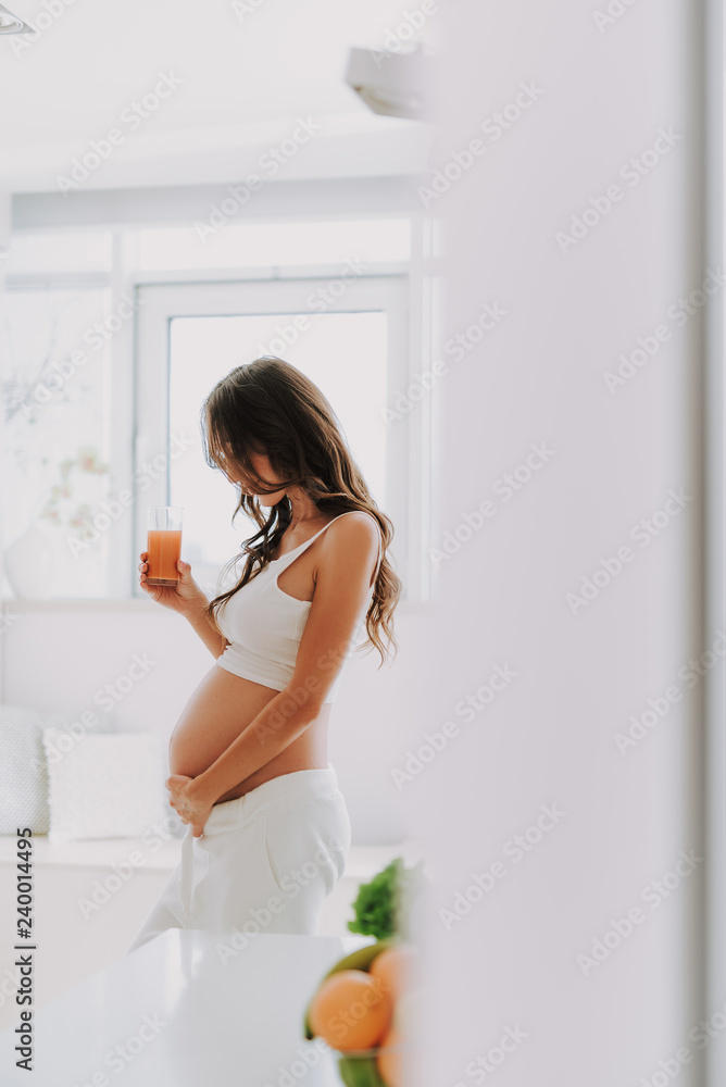 Pretty future mom looking at belly and holding juice in hand Pretty future mom looking at belly and holding juice in hand