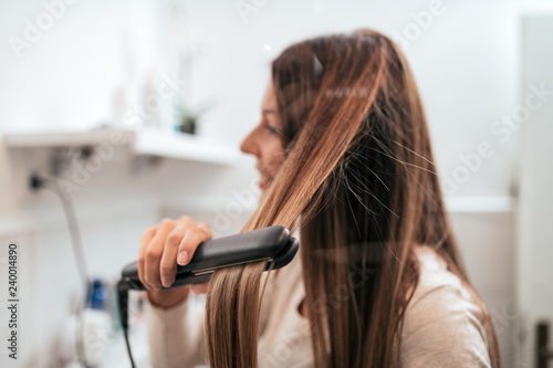 Young woman straightening her hair in the bathroom. photo