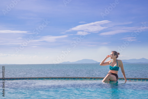 Outdoor summer portrait of young pretty woman looking to the ocean at tropical beach, enjoy her freedom and fresh air, wearing stylish hat and bikini