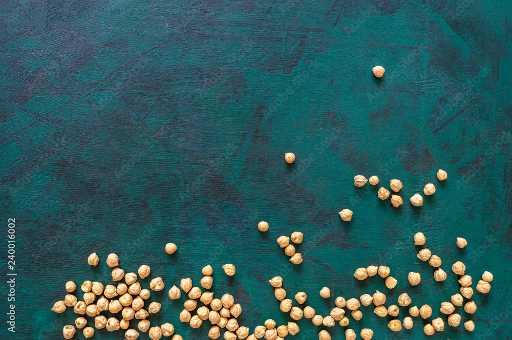 Dry chickpea beans are freely scattered on an emerald green background. Dry chickpea beans are freely scattered on an emerald green background.