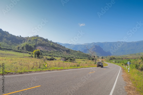 Scenic highway route 1148, view of a 4x4 truck on the road around with green meadow, mountain and blue sky background, Tham Sakoen National Park, Nan, northern of Thailand.