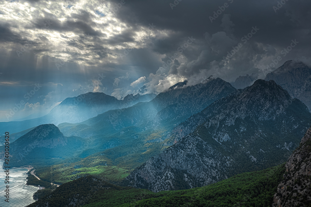 Amazing beautiful mountain landscape with charming clouds and soft sun rays falling down on earth through thick clouds. Nature background. Horizontal color photography.