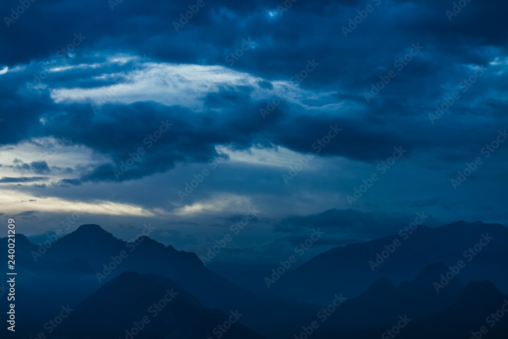 Amazing night landscape of calm clouds, blue sky and silhouettes of high mountains. Horizontal color photography.