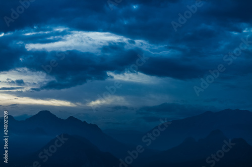 Amazing night landscape of calm clouds, blue sky and silhouettes of high mountains. Horizontal color photography.