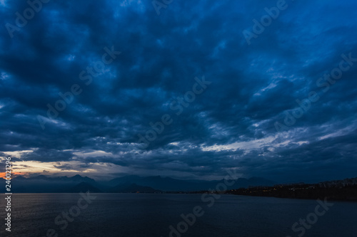 Beautiful sunset cloudy sky and dark sea water with silhouettes of mountains in background. Night is coming. Horizontal color photography.