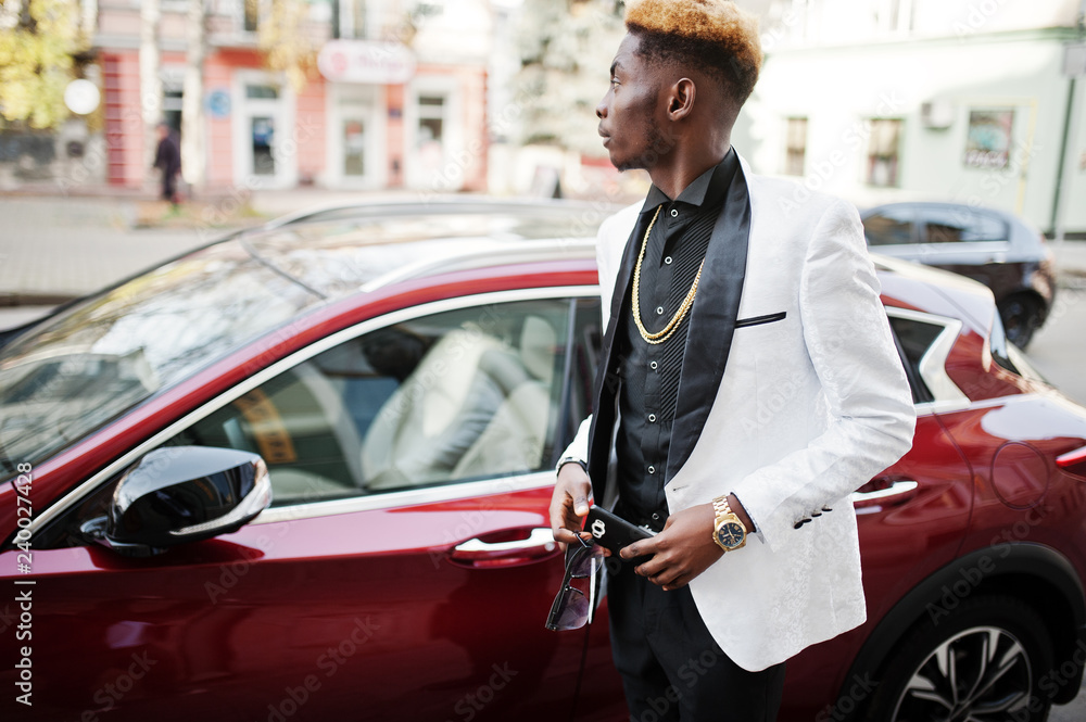 Chic handsome african american man in white suit against red luxury car with mobile phone at hand.