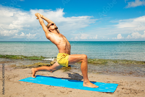 athletic man on beach doing fitness yoga exercise. Acroyoga element for strength and balance.