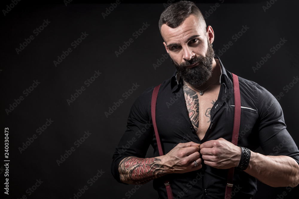 Foto Stock Uomo muscoloso tatuato con camicia bianca e bretelle rosse  chiude i pugni deciso su sfondo nero | Adobe Stock