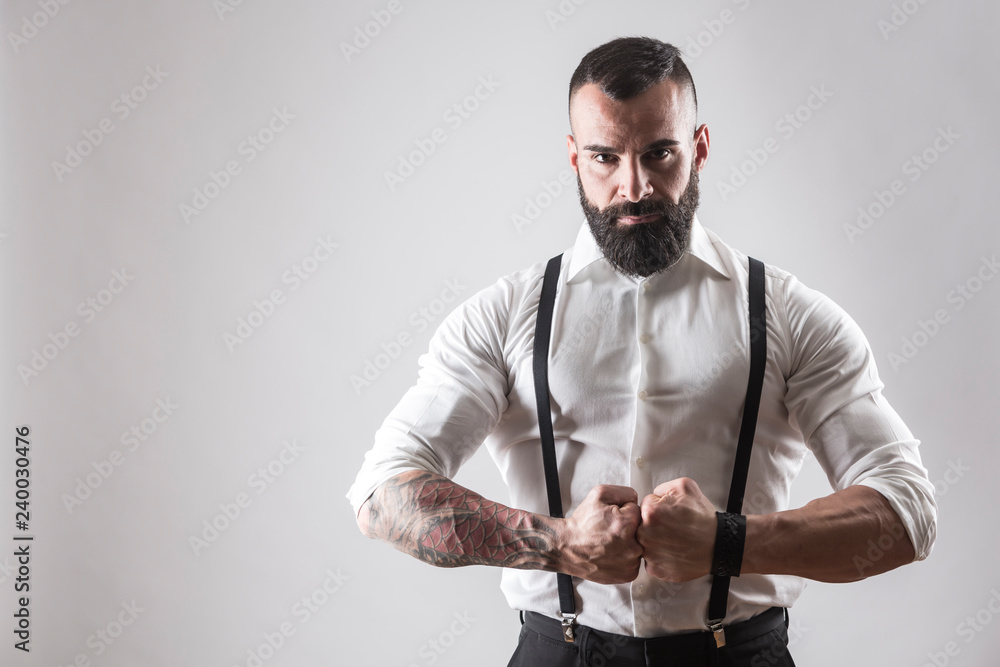 Uomo muscoloso tatuato con camicia bianca e bretelle chiude i pugni deciso  su sfondo bianco Stock Photo | Adobe Stock