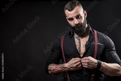 Uomo muscoloso tatuato  con camicia bianca e bretelle rosse chiude i pugni deciso su sfondo nero photo