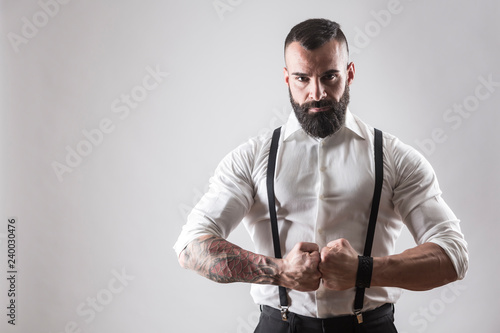 Uomo muscoloso tatuato  con camicia bianca e bretelle chiude i pugni deciso su sfondo bianco photo