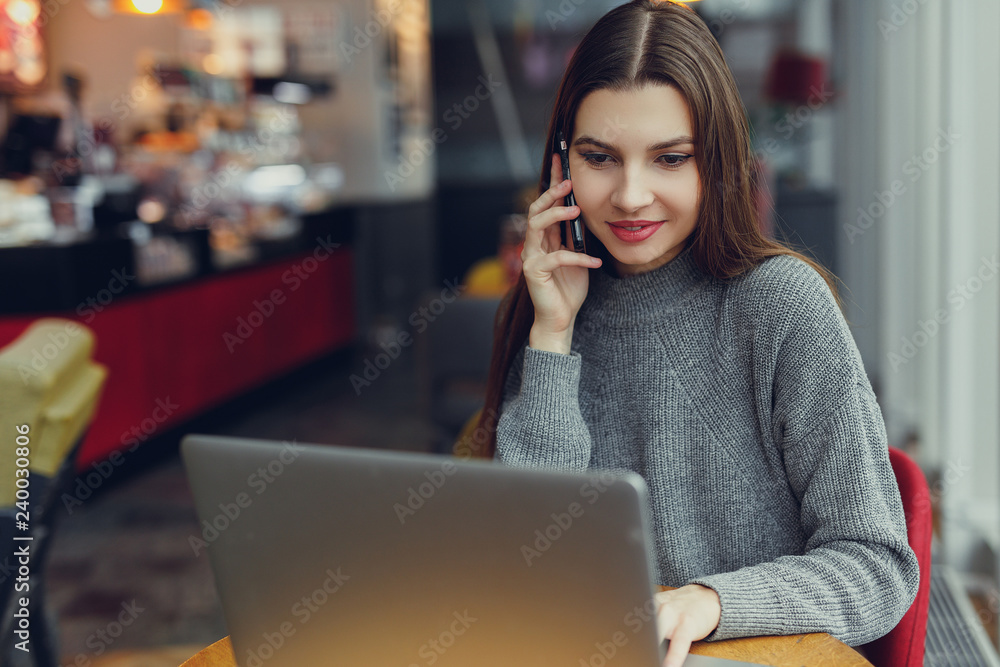 Down view. Young business woman sitting at table and talk at her phone while looking at laptop. Woman working at cafe. Blogger. - Image Down view. Young business woman sitting at table and talk at her phone while looking at laptop. Woman working at cafe. Blogger. - Image