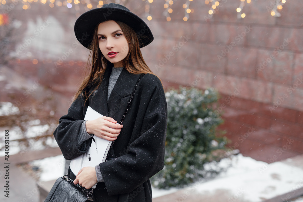 Young fashion woman hold her magazine, walk on the city street wear black hat look around and smile to camera. Copy space. - Image Young fashion woman hold her magazine, walk on the city street wear black hat look around and smile to camera. Copy space. - Image