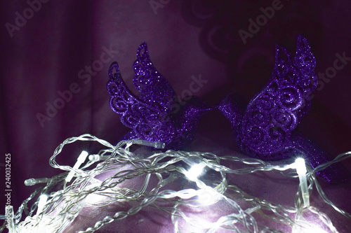 Two beautiful violet birds Christmas tree toys in the dark sparkle, shine, look at each other in the background white lights