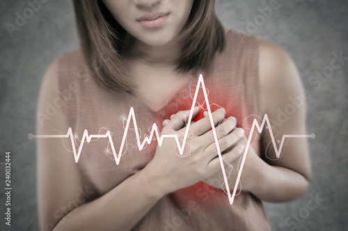 The Asian woman suffering from chest pain on a cement wall background. People having heart disease or heart attack. Hands pressing on the chest with a painful Because of Severe angina symptom photo