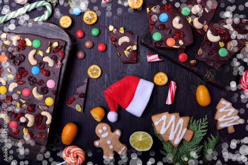 Santa Claus hat surrounded by chocolate, gingerbread cookies, citrus fruits and candy canes. Christmas composition
