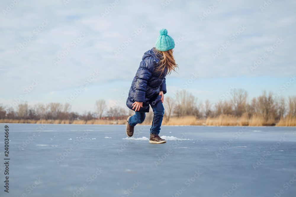Cute little girl wearing navy jacket and knitted hat walking in winter park. Pretty child playing and jumping on frozen lake. Family vacation with kid on christmas holidays Cute little girl wearing navy jacket and knitted hat walking in winter park. Pretty child playing and jumping on frozen lake. Family vacation with kid on christmas holidays