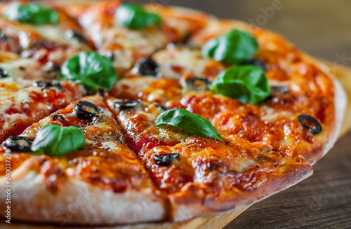 sliced Pizza with Mozzarella cheese, Tomatoes, pepper, olive, Spices and Fresh Basil. Italian pizza. Pizza Margherita or Margarita on wooden table background