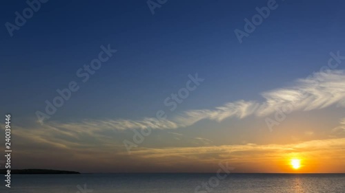 4k timelapse clouds crossing the amazing sky over the sea or ocean at sunset. Sun rays emerge through the clouds. The clouds cross slowly from right to left and appear to be orange blue and purple. 