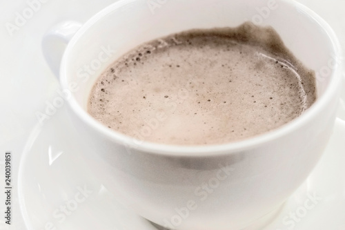 White cup of cocoa with froth on a saucer close-up