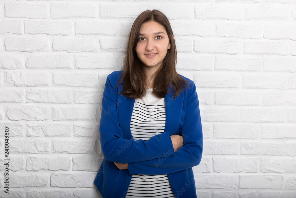 A young pretty smiling girl against a white loft-style brick wall. She looks at the viewer. Copy space. A young pretty smiling girl against a white loft-style brick wall. She looks at the viewer. Copy space.