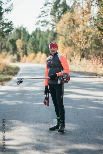 Training an athlete on the roller skaters. Biathlon ride on the roller skis with ski poles, in the helmet. Autumn workout. Roller sport. The athlete goes and holds sports equipment in his hand.