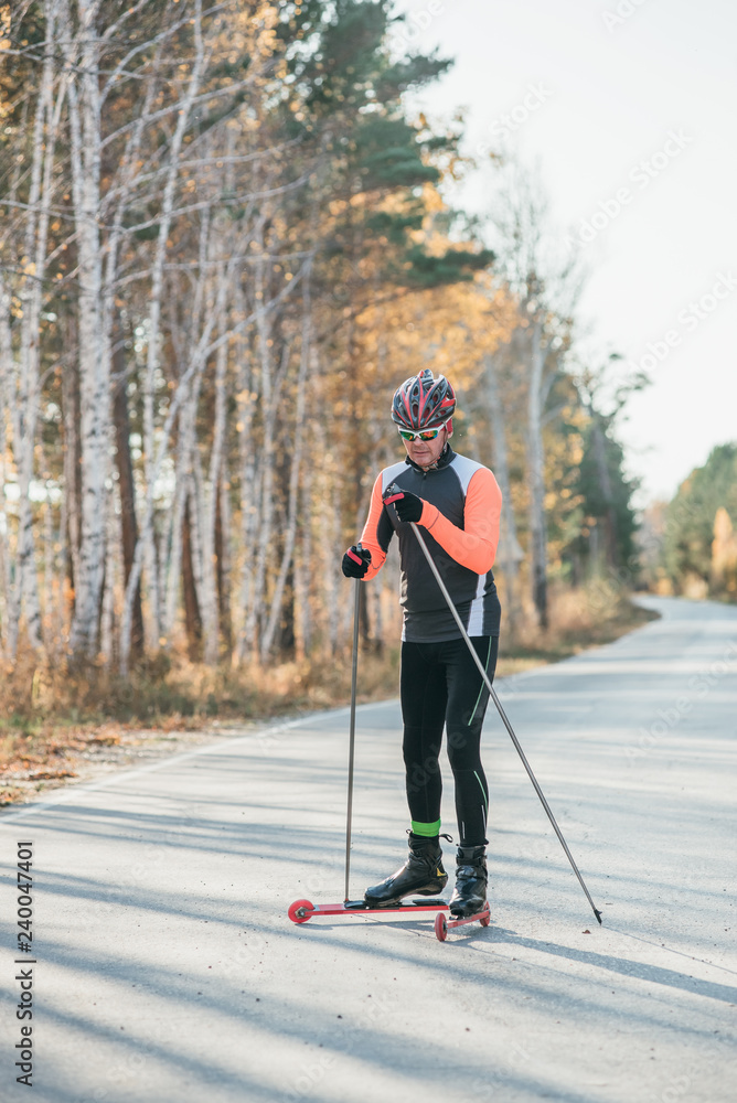 Training an athlete on the roller skaters. Biathlon ride on the roller skis with ski poles, in the helmet. Autumn workout. Roller sport. Training an athlete on the roller skaters. Biathlon ride on the roller skis with ski poles, in the helmet. Autumn workout. Roller sport.