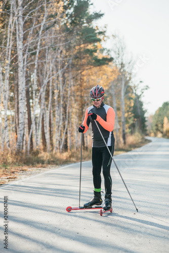 Training an athlete on the roller skaters. Biathlon ride on the roller skis with ski poles, in the helmet. Autumn workout. Roller sport.