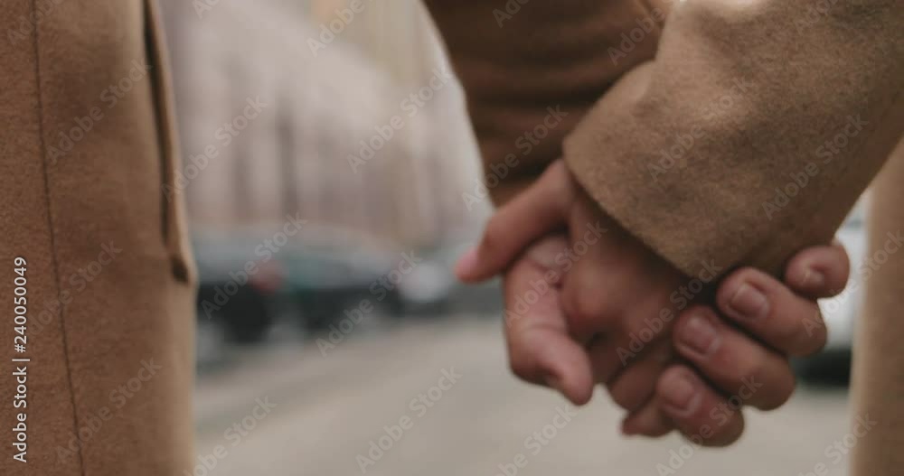Close up of the Caucasian holding hands in coats of the man and woman while they walking the street. Outdoor. Close up of the Caucasian holding hands in coats of the man and woman while they walking the street. Outdoor.