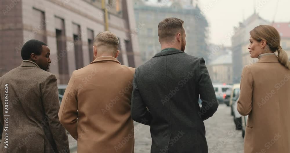 Back view on the team of the multiethnic successful people businessmen and businesswoman walking the street joyfully and talking. Rear. Outdoors. Back view on the team of the multiethnic successful people businessmen and businesswoman walking the street joyfully and talking. Rear. Outdoors.