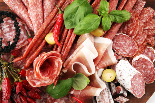 Food tray with delicious salami, pieces of sliced prosciutto crudo, sausage and basil. Meat platter with selection