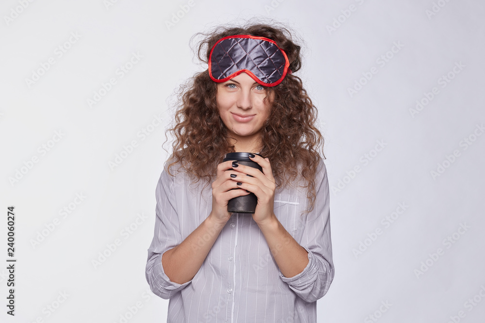 Φωτογραφία Pleased female glad to receive coffee at bed from lover, dressed in casual grey pajamas, has sleeping mask on head, has good sleep, isolated over white studio wall